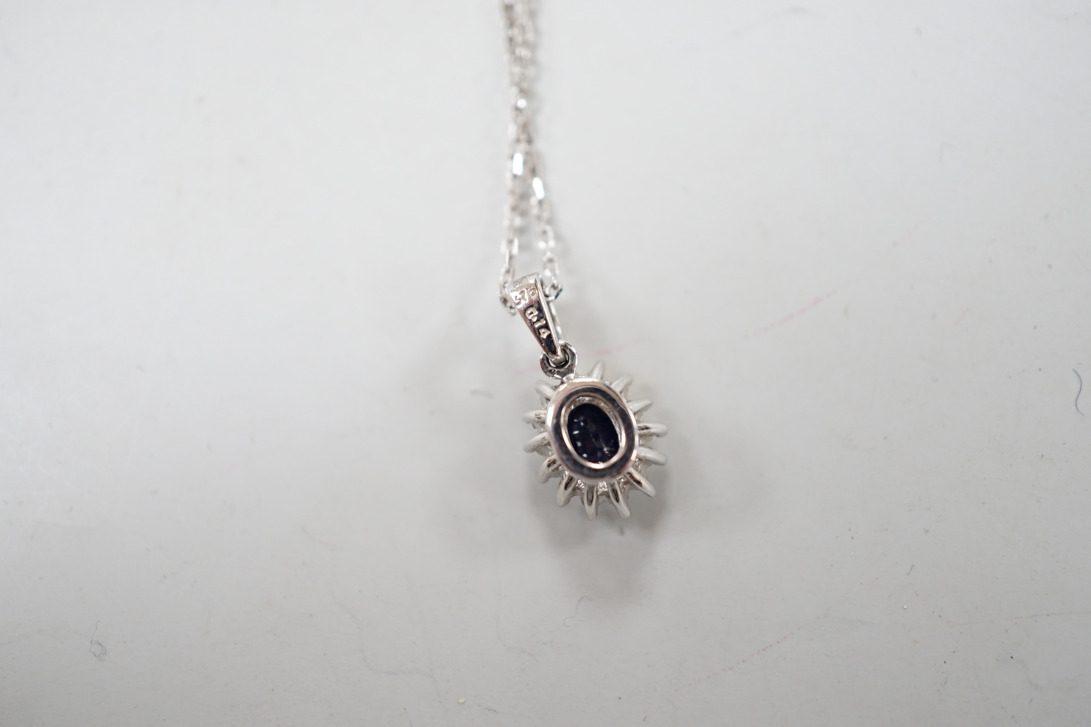 A modern 9ct white gold, sapphire and diamond set oval cluster pendant, overall 15mm,on a modern 9ct white gold chain, 40cm, gross weight 2.8 grams.